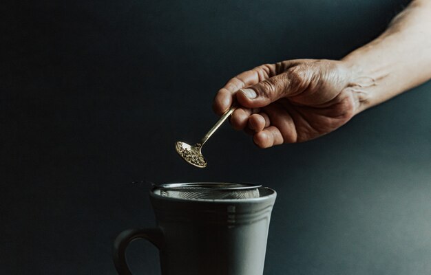 Una mano vieja preparando un té sobre un fondo oscuro y tonos oscuros