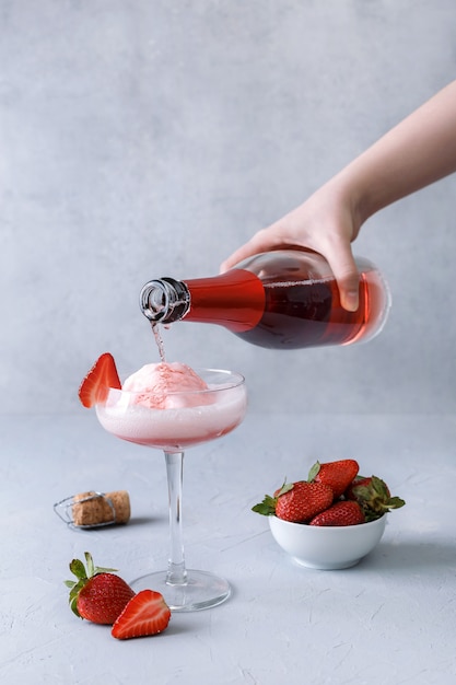 La mano vierte champán rosado en un vaso con helado de fresa sobre una superficie gris. El concepto de deliciosas bebidas. Copia espacio