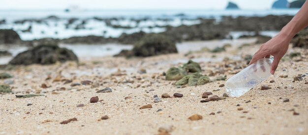 Mano voluntaria recoger basura Botella de plástico basura en la playa Ecología Contaminación ambiental y concepto de problema ecológico