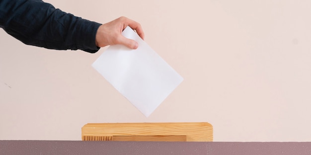 Una mano de votante puso papel en la urna, elección de democracia