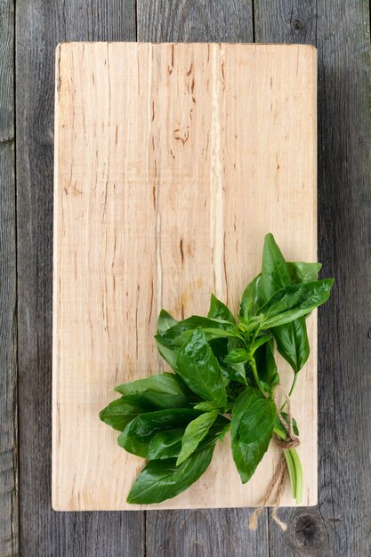 Manojo de albahaca fresca sobre un soporte de madera y una superficie de mesa vieja. Estilo rústico. Vista superior. Enfoque selectivo.