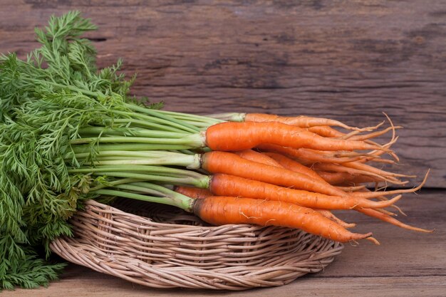 Manojo de zanahorias frescas con hojas verdes sobre fondo de madera