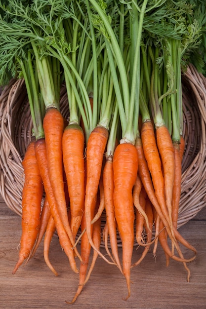 Manojo de zanahorias frescas con hojas verdes sobre fondo de madera