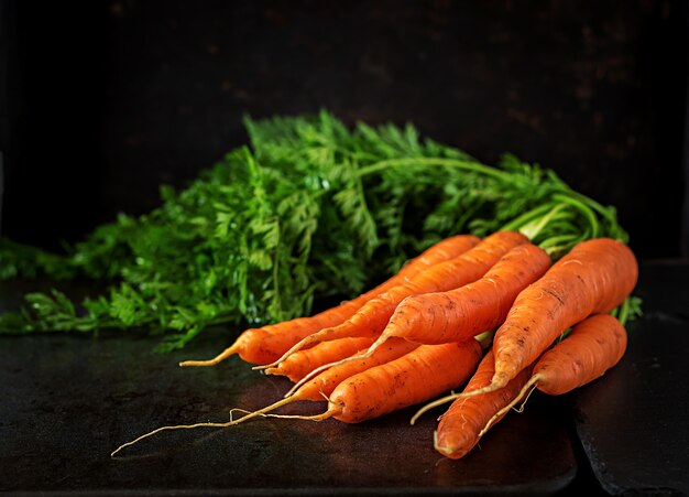 Manojo de zanahorias frescas con hojas verdes en la superficie oscura.