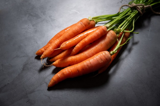 Manojo de zanahorias orgánicas, con sus tallos verdes sobre un fondo gris, visto de lado