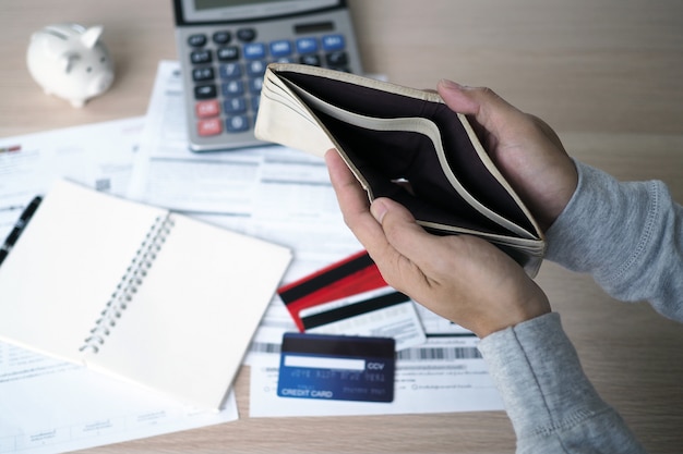 Las manos abren el bolso vacío después de calcular el costo de la tarjeta de crédito y la factura.