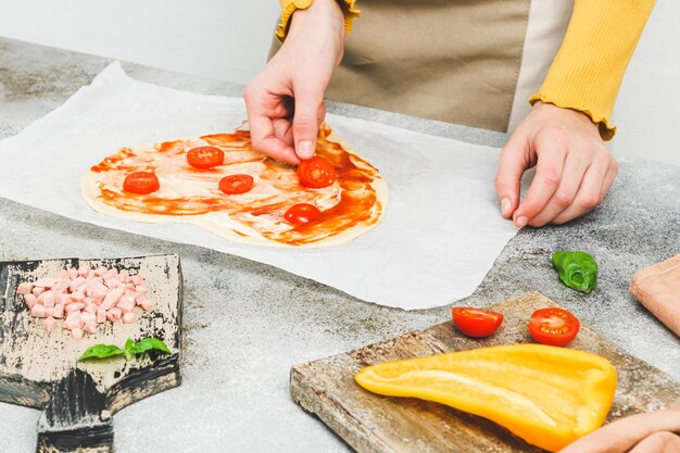 Las manos de una adolescente caucásica colocan rodajas de tomate cherry sobre masa de pizza en forma de corazón