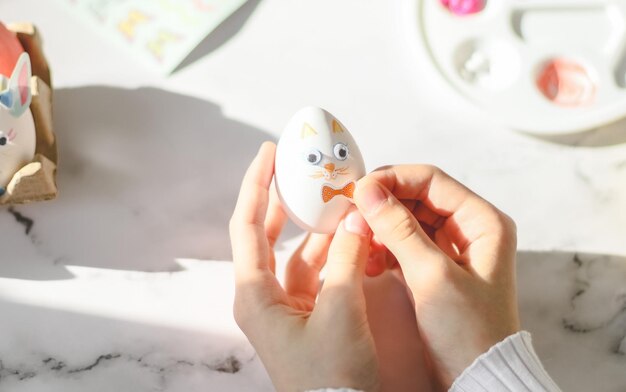 Manos de una adolescente caucásica con cuello alto blanco sosteniendo un huevo de conejito de Pascua y pegando un lazo adhesivo