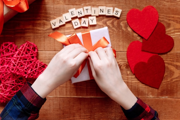 Foto manos de un adolescente preparando un regalo para el día de san valentín sobre un fondo de madera. corazones y decoración navideña.