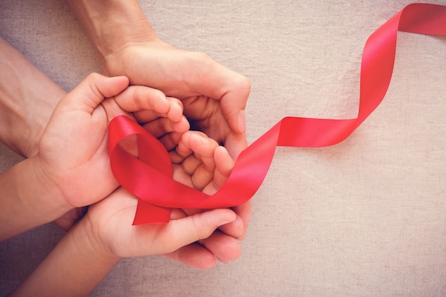 Manos de adultos y niños con cinta roja, Día Mundial del SIDA.