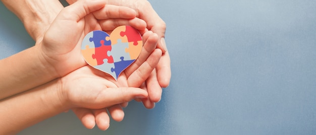 Manos de adultos y niños con rompecabezas en forma de corazón, conciencia del autismo, concepto de apoyo familiar del espectro autista, Día Mundial de la Concienciación sobre el Autismo