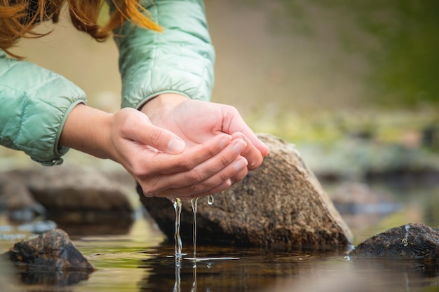 Foto manos y agua primer plano de una mujer tomando agua de un lago de montaña en sus manos