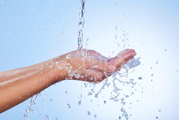 Foto manos con agua salpicada y lavado para la higiene del cuidado de la piel o hidratación contra un fondo de estudio azul primer plano de la mano con gotas de líquido ducharse o lavarse para un bienestar limpio o sostenibilidad natural