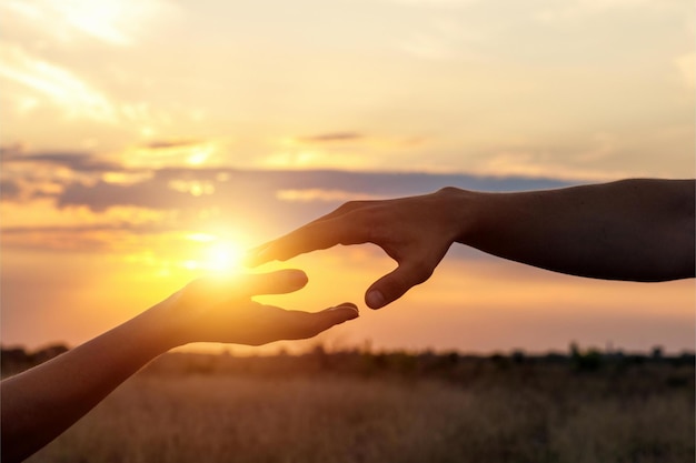 Las manos se alcanzan en el fondo de la puesta de sol