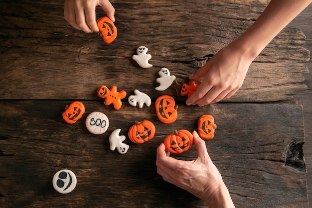 Foto las manos alcanzan el pan de jengibre de halloween en forma de calabazas fantasmas y hombre de pan de jengibre sobre fondo de madera