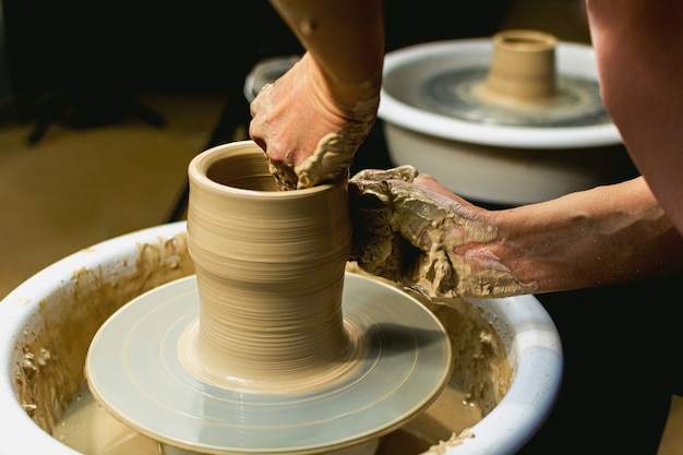 Las manos de la alfarera formadas por una vasija de barro sobre un torno de alfarero. El alfarero trabaja en un taller. Foto de alta calidad