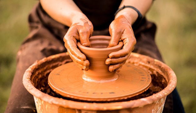 Manos de alfarero hacen jarra de cerámica en torno de alfarería enfoque selectivo exterior