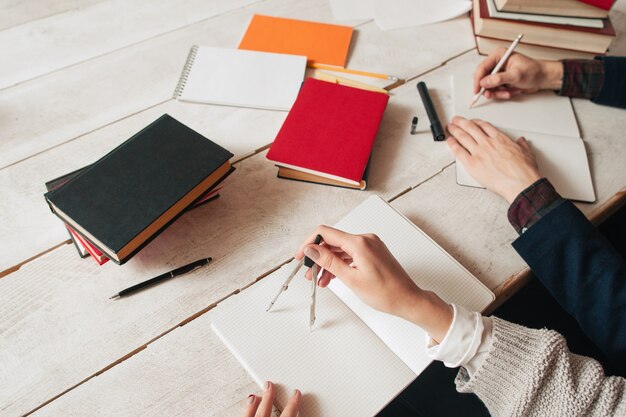 Manos de alumnos que estudian matemáticas en un escritorio con suministros