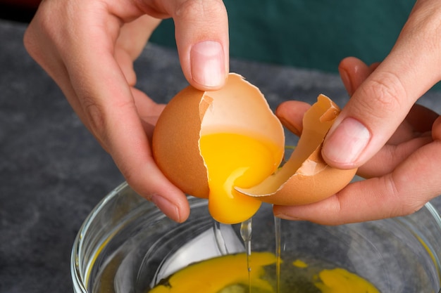 las manos de la ama de casa o el chef rompiendo la yema de huevo fresca y cayendo en un cuenco