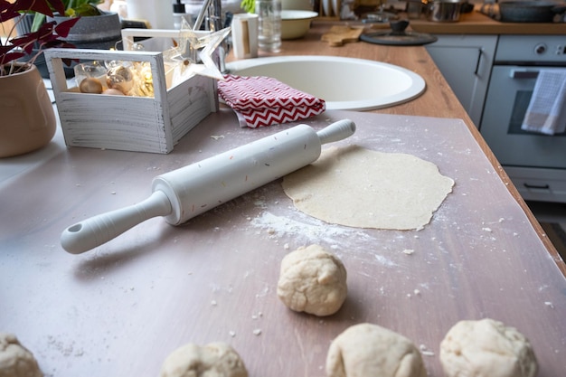 Las manos amasan masa gruesa con un rodillo en la mesa de la cocina decorada con decoraciones festivas para Navidad y Año Nuevo Hornear en casa aroma y comodidad