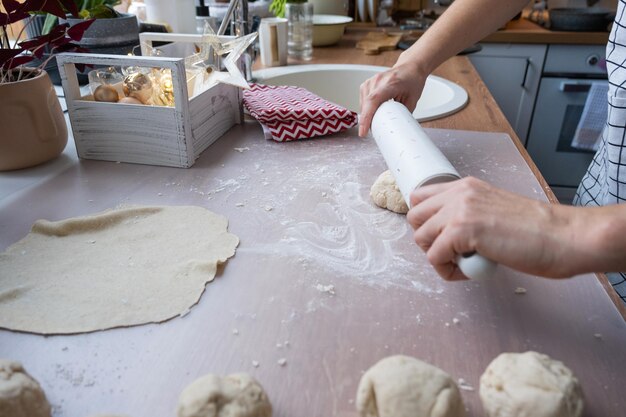 Las manos amasan masa gruesa con un rodillo en la mesa de la cocina decorada con decoraciones festivas para Navidad y Año Nuevo Hornear en casa aroma y comodidad