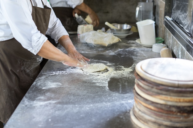 Manos amasando la masa para la fabricación de pizza, chef preparando la base para hacer italiano tradicional