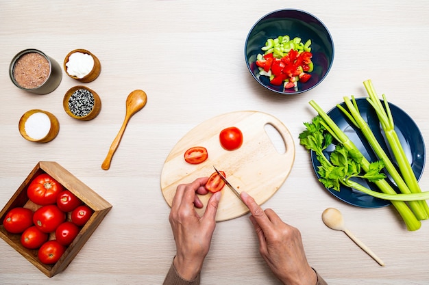 Manos de una anciana mientras cocina ensalada con apio, tomate y atún en una mesa de madera