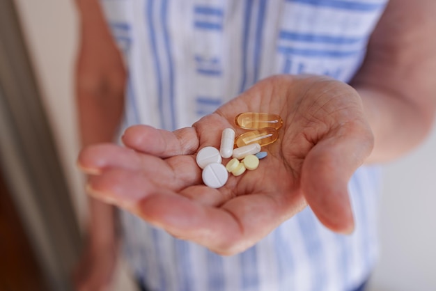 En manos de una anciana un puñado de varias pastillas y vitaminas