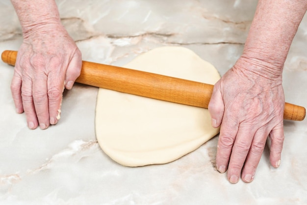 Las manos de la anciana ruedan la masa sobre la mesa