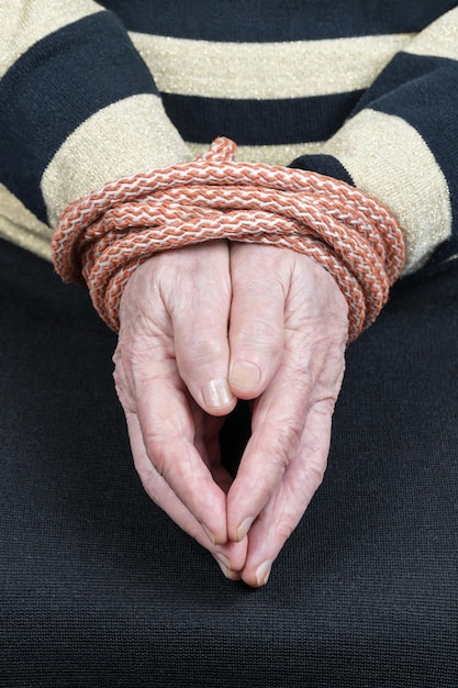 Manos de una anciana sentada en una silla atada con una cuerda cerrada