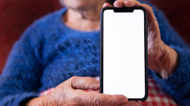 Las manos de una anciana sostienen un teléfono inteligente con una pantalla blanca vacía para tu maqueta