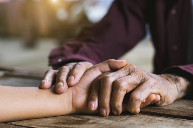 Manos del anciano y una mano de hombre en la mesa de madera