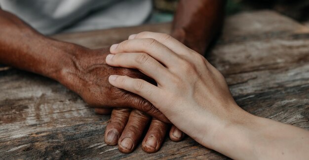 Manos del anciano y una mano de mujer en la mesa de madera a la luz del sol