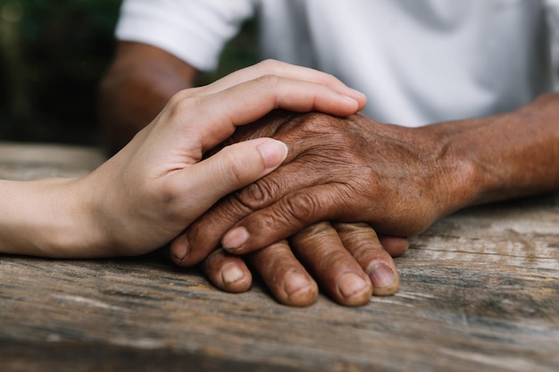 Manos del anciano y una mano de mujer en la mesa de madera