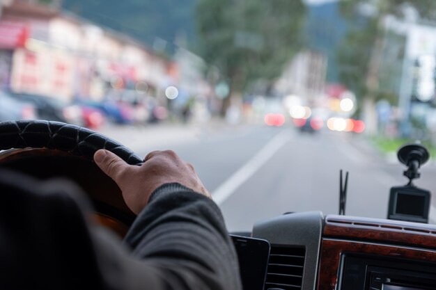 manos de un anciano mientras conduce en la carretera con luces borrosas y tráfico de coches