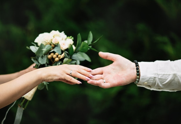 Manos con anillos de boda y ramo Fondo verde