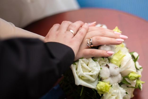 Manos con anillos de boda en un ramo de rosas blancas