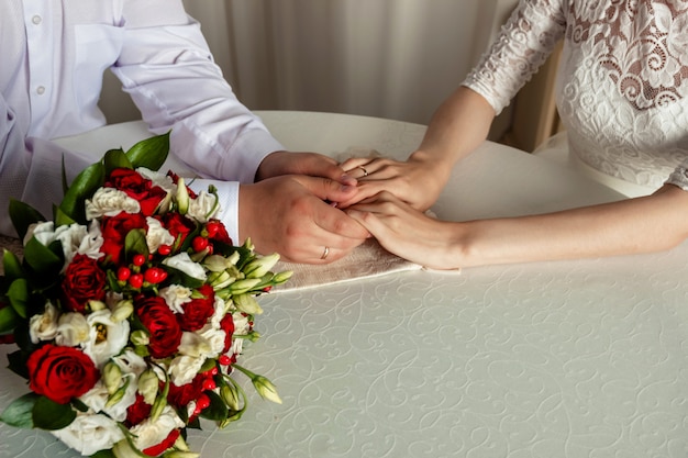 Foto manos y anillos de pareja recién casada con ramo de novia.