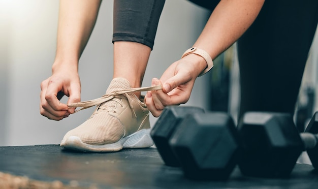 Las manos de la aptitud o la mujer atan los zapatos antes de comenzar el ejercicio con mancuernas, el entrenamiento en el gimnasio o el entrenamiento deportivo, el bienestar de la salud y las piernas de la atleta o la persona se preparan para el desafío del rendimiento cardiovascular