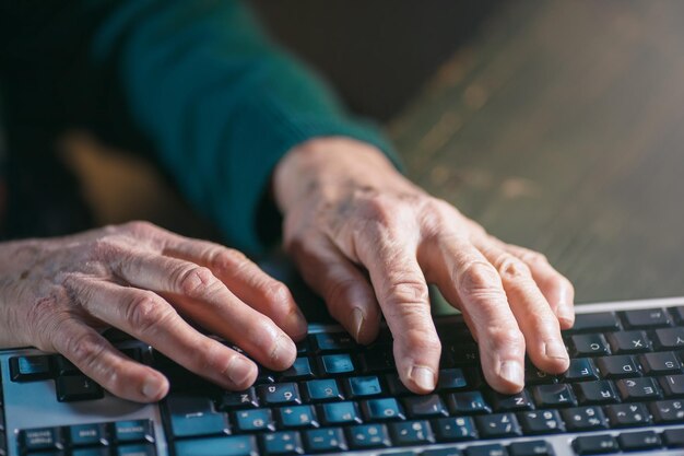 Manos arrugadas recortadas usando el teclado de la computadora en la mesa