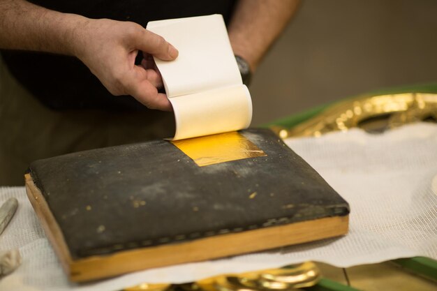 Manos de artesano trabajando con una hoja de oro.