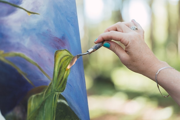 Foto manos del artista pintando su obra al aire libre.