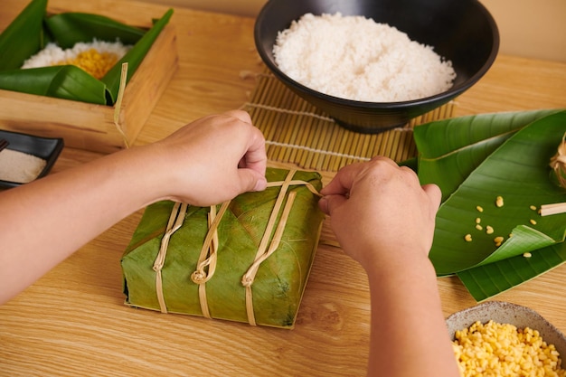 Manos atando pastel cuadrado vietnamita envuelto con cuerdas de bambú