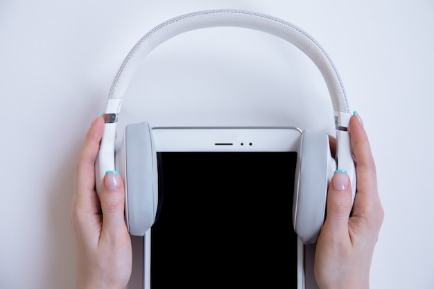 Foto en las manos, los auriculares blancos se colocan en una tableta blanca sobre un fondo blanco.