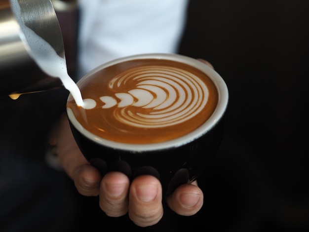 manos de barista verter leche tibia para hacer café con leche arte.