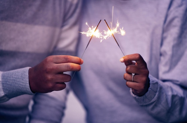 Manos de bengalas y celebración de pareja con luces chispas y magia para la noche de año nuevo amor y aniversario Primer hombre mujer y personas celebran con destellos fuegos artificiales y brillan con brillo