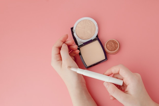 Manos de blogger de belleza de mujer sosteniendo botella y tubo spa cosméticos profesionales de alta gama sobre fondo rosa, concepto de minimalismo, cálidos tonos acogedores y copyspace