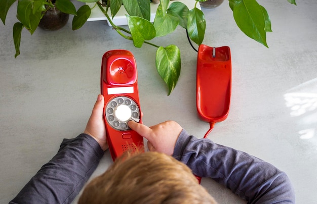 manos y cabello de un niño usando un teléfono rojo antiguo en su hogar concepto de cambios tecnológicos