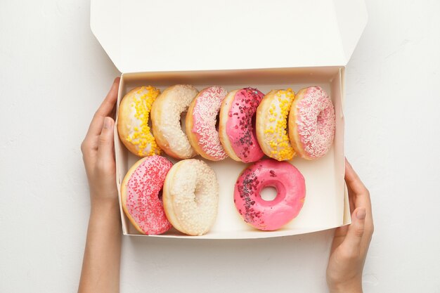 Manos con caja de donas dulces en pared blanca