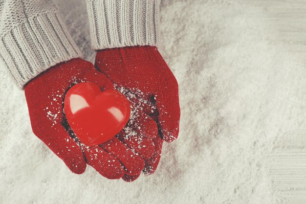 Manos en cálidos guantes rojos sosteniendo el corazón sobre fondo nevado